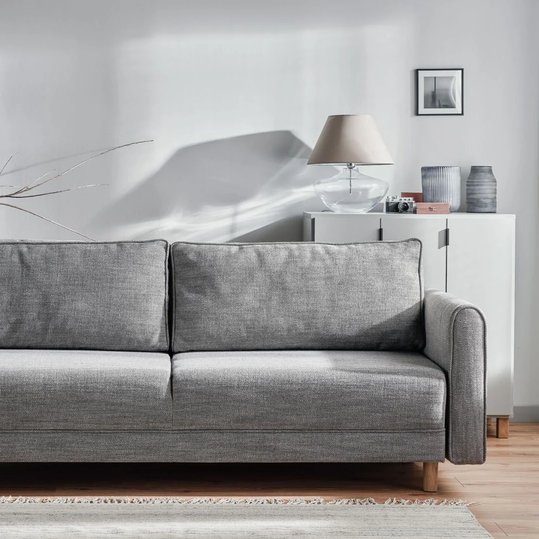 Szara sofa w jasnym salonie z delikatnymi dekoracjami.